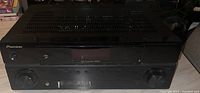 Front and top view of the Pioneer surround sound receiver showing the control knobs, buttons, digital display, and ventilation slots.