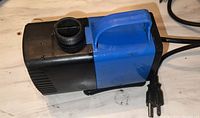 Photo of the submersible pump showing black and blue body, handle, power cord with two-prong plug, and water outlet.