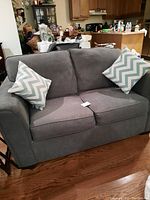 Front view of grey fabric 2 seater sofa with two blue and white chevron patterned pillows on each side.