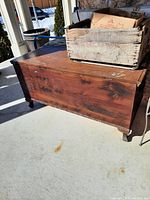 Antique wooden hope chest with visible wear and patina placed outdoors on concrete surface
