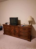 Wooden low cabinet against beige wall featuring six drawers and central folding doors concealing four drawers. Items on top like TV and lamp are not included.