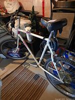 White adult bicycle seen from side in basement setting showing frame, tires, and black seat labeled BOSS.