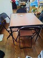 Photo showing the card table set up with four folding chairs around it on a wooden floor.