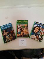 Three Cherry Ames paperback books with colorful illustrated covers placed side by side on white surface