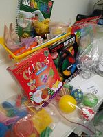 Photo showing a yellow bin filled with assorted children's toys including building blocks, bouncing balls, electronic Simon Says game, bubble book, and mini Angry Birds puzzle