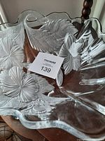 Clear crystal bowl with floral and leaf pattern on wooden table, showing scalloped edges and detailed engraving.