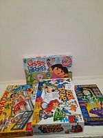 Four boxed games stacked, showing Operation, Mouse Trap, Hangman and Chutes and Ladders Dora the Explorer edition