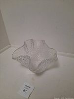 Clear glass bowl with textured pattern and wavy edges placed on a white surface.
