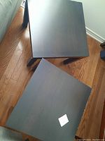 Top view of two black square IKEA tables showing surface wear