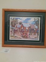 Photo of framed Jill Walker painting showing house at Lower Carleton, St. James, Barbados with people and palm trees.
