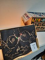 Photo of Lite-Brite board in use with lit pegs forming a cat and text, box partially visible in background