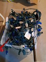 Photo displaying a tangled bundle of outdoor Christmas lights with green wiring and blue and white/clear bulbs lying on top of a white plastic bin.