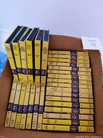 View of 34 Nancy Drew Mystery Stories hardcover books in a cardboard box showing yellow spines and Grosset & Dunlap logo with mostly intact condition.