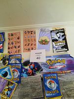 Pokemon card lot with two sheets of Pokemon stickers, a Pokemon Black & White card pack or promo, and a Pokemon play mat showing the Bench area with character artwork.
