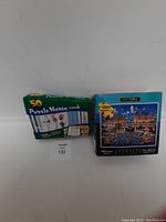Photo shows two boxed puzzle sets: a 1000 piece Ottawa puzzle and a 50 card Puzzle Mania brainteaser set, both new.