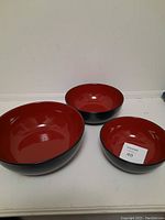 Set of three red interior and black exterior bowls of varying sizes placed on table.