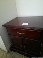 Top and front angle view of wooden side table showing drawer and cabinet doors with brass handles.