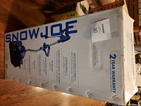 Box showing Snow Joe brand name, product specifications, and 2 year warranty on snow blower/shovel.