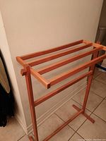 Photo of teak shower rack showing wooden structure with three top slats and vertical supports against a tiled floor and wall.
