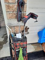 Photo of vintage golf bag and clubs showing the bag's red and black plaid pattern, green towel hanging, and various clubs with wood and metal heads.