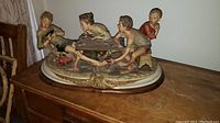 Full view of the Capodimonte porcelain figural group showing four boys playing cards on an oval base with gold detailing.