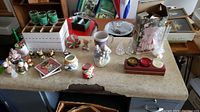 Overview of mixed Christmas figurines, candle holders, votive holders, bell, and albums laid out on a table