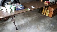 Full view of the folding table showing length, metal legs, and woodgrain surface with items on top for scale.