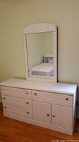 Front view of the white child's long dresser with colorful knobs and arched detachable mirror above it.