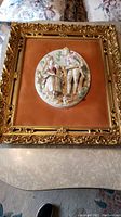 Photo of one porcelain relief art piece showing boy and girl on velvet background in ornate gold frame