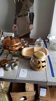 Photo showing copper fondue set, glass jars and candy dish, ceramic urn, divided serving dish, and candle tins on a table.