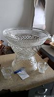 Clear pressed glass punch bowl with diamond and hobnail pattern, shown on countertop with small glasses.