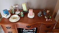Photo of a wooden desk with various decorative items: Royal Doulton Bunnykins ceramic bowl and plate, angel and cherub candle holders with candles, violin themed figurines, light-up violin decoration, and small ceramic animal figurines.