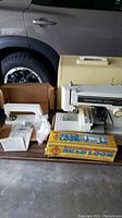 Photo showing vintage Kenmore 158 sewing machine with hard case, bead loom box, and bedazzler craft kit on table.