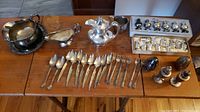Photo showing multiple silver plated spoons and forks, sterling silver salt and pepper shakers, a silver plated gravy boat, a serving bowl, and a Reed & Barton silver soldered item.