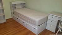 White twin size platform bed with mattress, bookcase headboard, and storage drawers underneath.