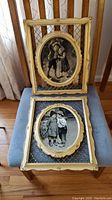 Two oval artworks of children in cream decorative frames on metal lattice backgrounds, displayed on a blue padded chair with wooden slats behind.