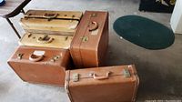 Five vintage suitcases stacked and arranged on floor, showing their overall condition and color tones.
