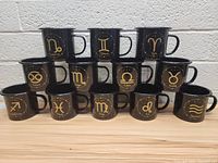 Set of 12 black enamel birth sign mugs arranged in a pyramid