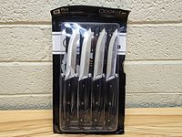 Packaged CookiT steak knives, set of 3 knives shown in front packaging with black handles and stainless blades.