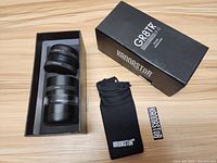 Kannastor GR8TR V2 Medium grinder inside box with black storage pouch and Kannastor sticker beside it on wooden surface.