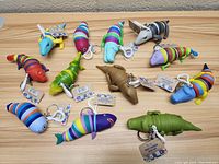 Top-down view of 12 colorful segmented fidget crawler keychains laid flat on a wooden surface, showing their unique multi-colored silicone segmented bodies and clip attachments.