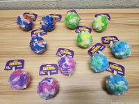 Top view of 12 LED light up bubble pop balls in assorted colors arranged on a wooden surface in mesh packaging with purple tags.