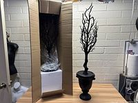 Wide view of one black Halloween decorative tree with twisted bare branches in a black urn pot next to boxed second tree.