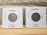 Two V-Nickel coins dated 1905 and 1906 in individual white cardboard holders labeled with the year and 'V-NICKEL'. Coins show obverse side with Liberty Head design visible.
