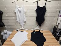 Four black and white women's tops hung on hangers and laid on table against brick wall background.