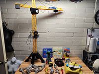 Overview photo of the large toy crane and assorted toys laid out on a table, including books, plush items, figurines, and small toys.
