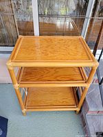 Full view of the 3-tier bamboo rattan shelf showing three wooden shelves and bamboo frame with rattan bindings.