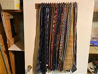 Photo showing approximately 14 men's tie lengths hanging on a metal rack, displayed against a white wall for clear visibility.