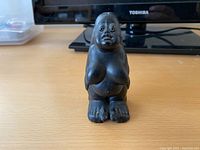 Front view of the black lava stone figurine showing seated female form with visible facial features and body contours.