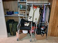 Image of vintage walker's padded seat with white shoes and black bag on top, alongside vintage naval vest and other clothing on hangers in background.